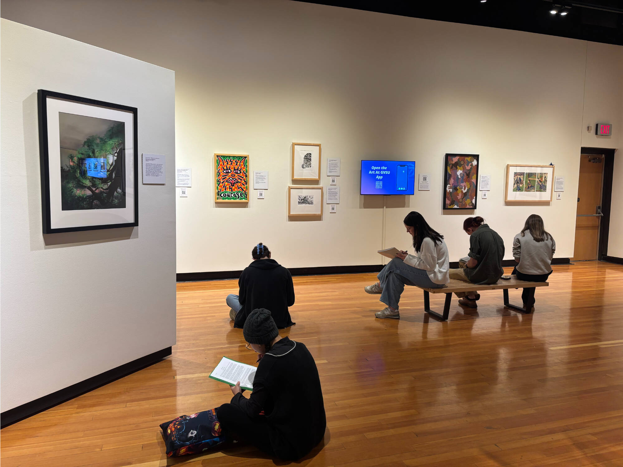 Photograph of students writing poetry surrounded by artwork in the GVSU Art Museum PAC Gallery.